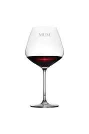A clear red wine glass with the word 'MUM' engraved on it, filled with red liquid, showcasing an elegant stem.