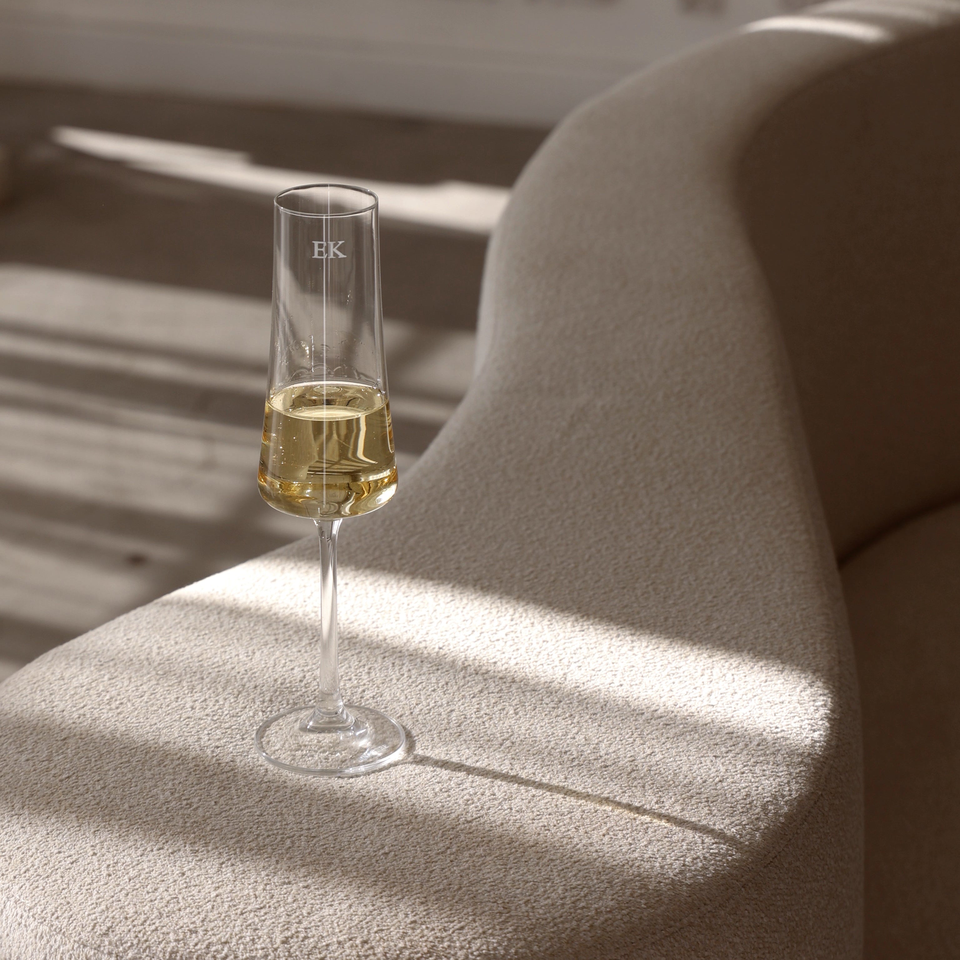 Single champagne Flute with initials 'EK' engraved on the arm of a white couch