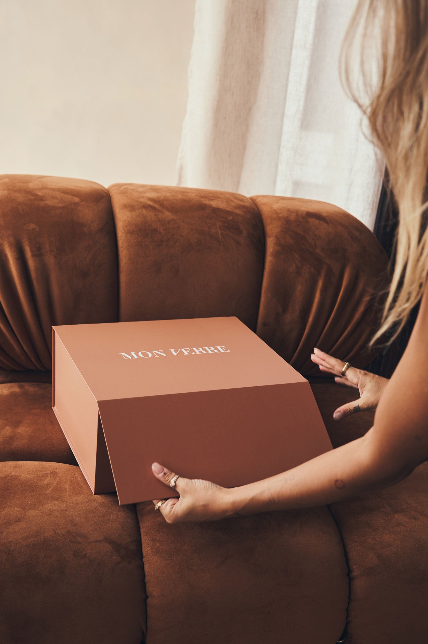 Person holding a brown box labeled 'MON VERRE' on a brown couch.