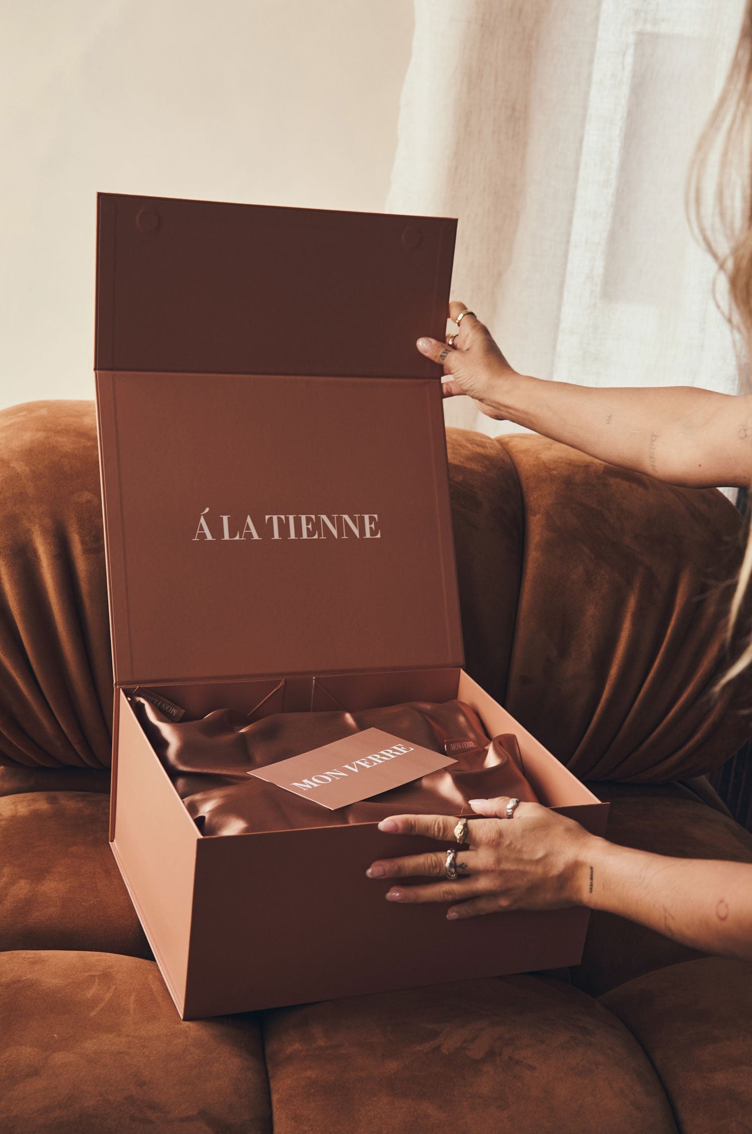 Person opening a brown 'ALATIENNE' box on a couch