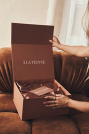 Person opening a brown 'ALATIENNE' box on a couch